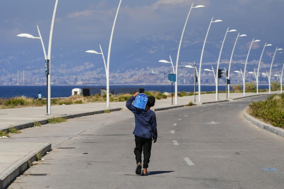 A young street vendor carries a pack of water bottles as he looking for customers during a sweltering day on the Mediterranean Sea corniche in Beirut, Lebanon, Thursday, July 20, 2023. (AP Photo/Hassan Ammar)