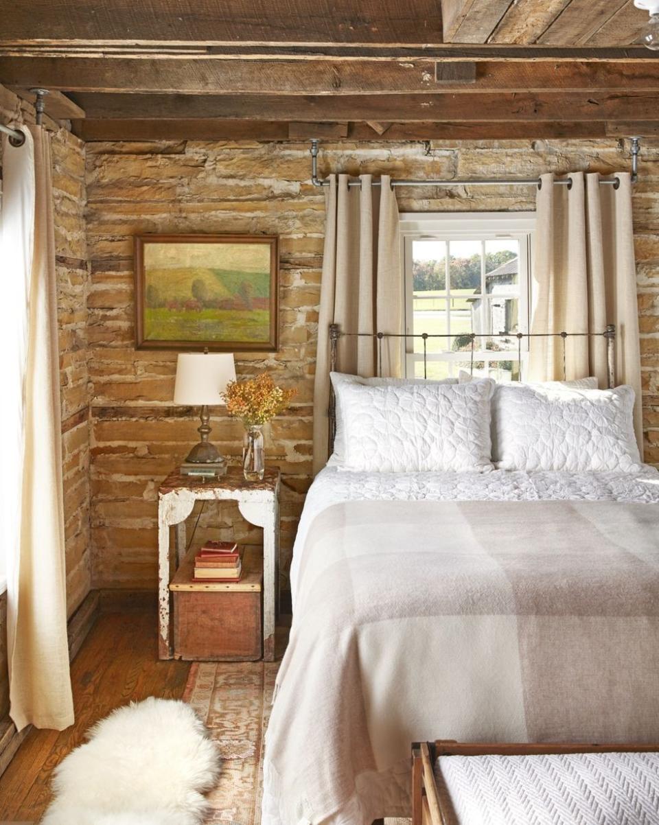 the wood slat walls and exposed ceiling in this master bedroom get an extra dose of humbleness with a chippy bedside table and weathered bed frame and simple yet comfortable bedding and a fluffy throw rug bring a layer of softness to the room