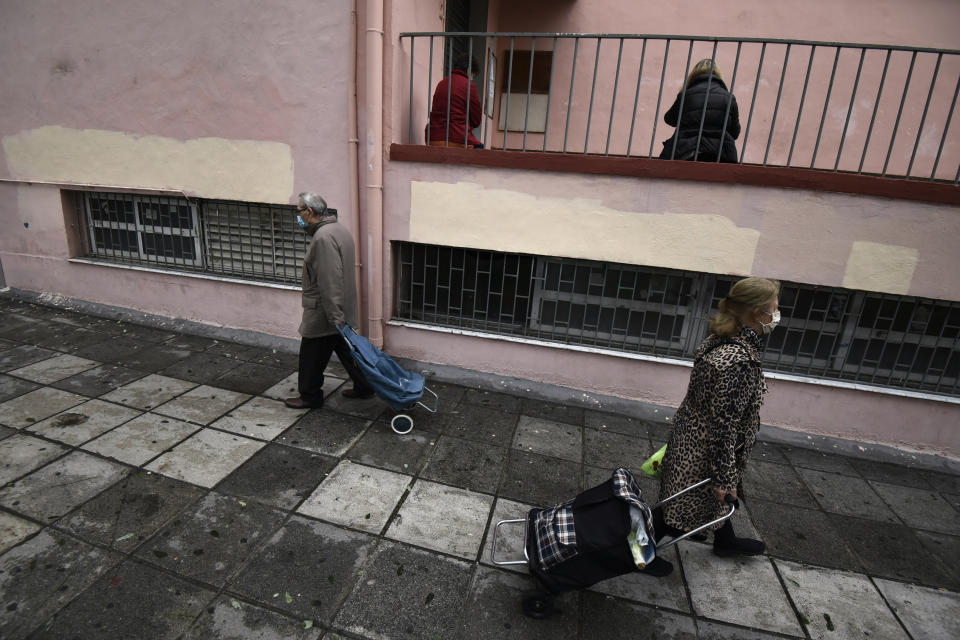 Two people wearing face masks against the spread of the coronavirus, pull their shopping trolleys outside a school during the lockdown to contain the spread of COVID-19 in the northern city of Thessaloniki, Greece, Tuesday, Nov. 3, 2020. Greece's government imposed a localized lockdown on its second largest city of Thessaloniki and the northern province of Serres, after major increases in the number of coronavirus infections there. (AP Photo/Giannis Papanikos)