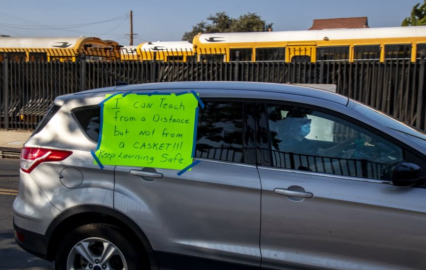 COMPTON, CA - OCTOBER 1 2020: A teacher drives by a lot filled with parked school buses with a sign saying "I can teach from a distance but not from a casket. Keep learn safe" while participating in a car caravan to protest against the Compton Unified School District for the reopening of schools despite what many teachers and community members say are unsafe conditions because of COVID-19 on October 1, 2020 in Compton, California. (Gina Ferazzi / Los Angeles Times)