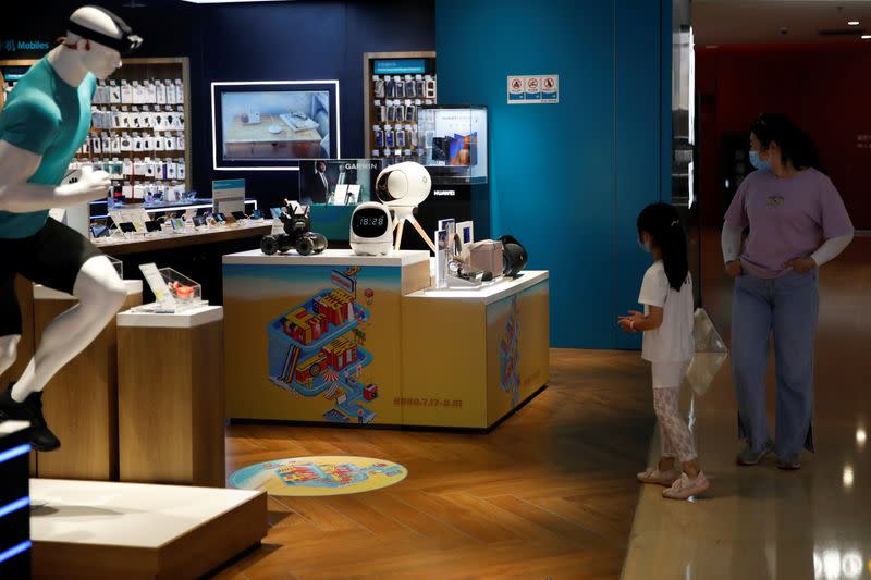 A woman and a girl wearing face masks look at the merchandise on an electronics store at a shopping mall, in Beijing