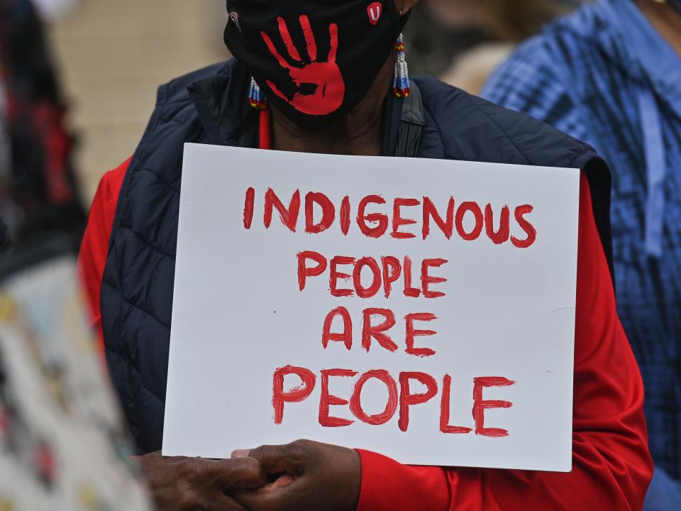 A participant holds a placard with words 'Indigenous People Are People.'