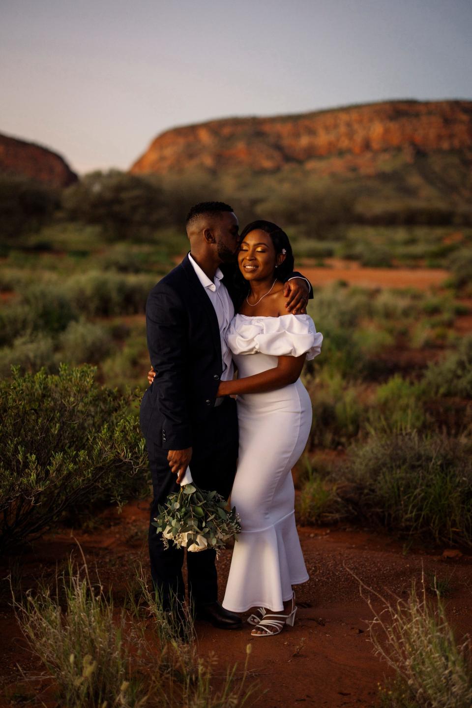 A bride and groom embrace in a field.