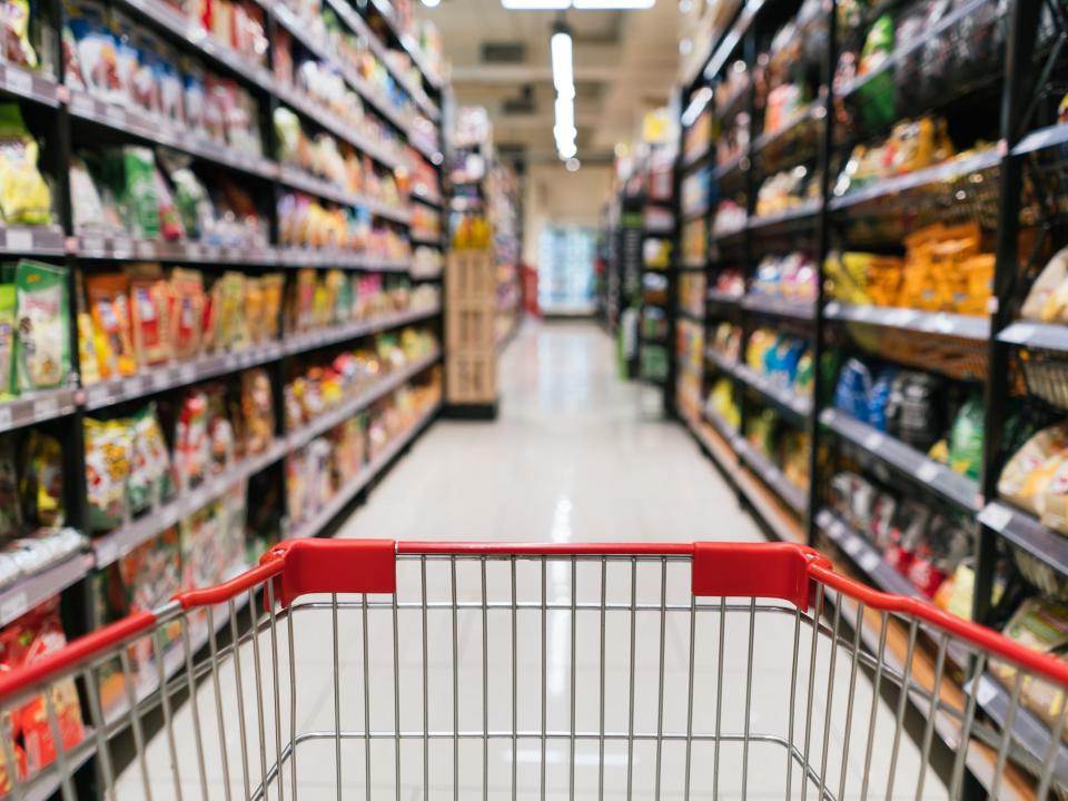 a view from the top of a grocery cart facing an aisle of chips, snacks and other processed foods in soft focus