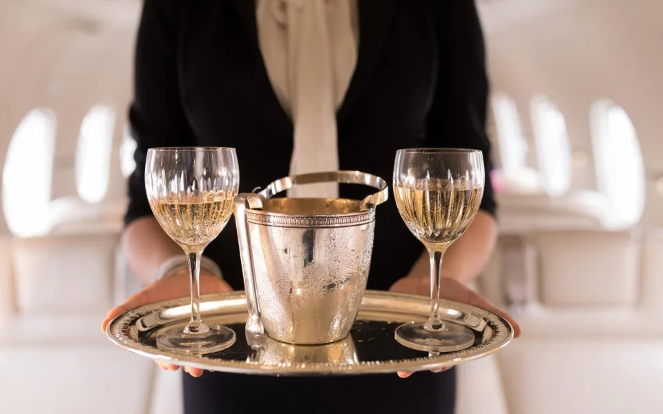 Flight attendant serving glasses of champagne in private jet - Alamy Stock Photo