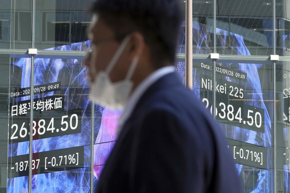 A person wearing a protective mask walks in front of an electronic stock board showing Japan's Nikkei 225 index at a securities firm Wednesday, Sept. 28, 2022, in Tokyo. Asian shares tumbled Wednesday after a wobbly day ended with mixed results on Wall Street as markets churn over the prospect of a possible recession. (AP Photo/Eugene Hoshiko)