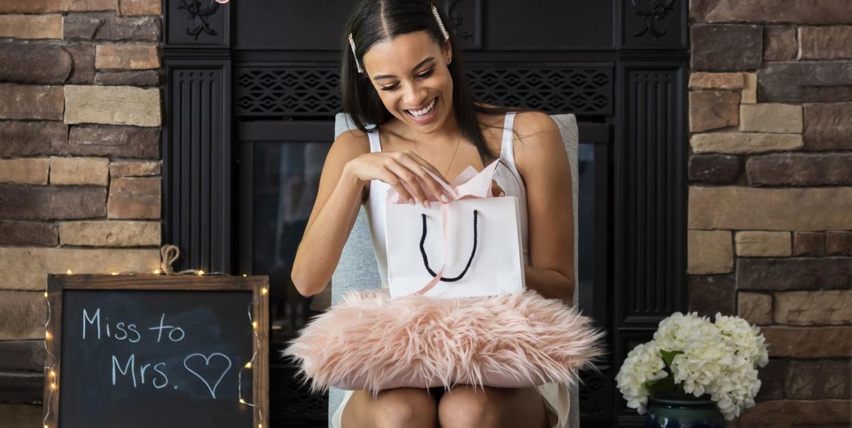 woman opening up gift at bridal shower under balloons that say bride