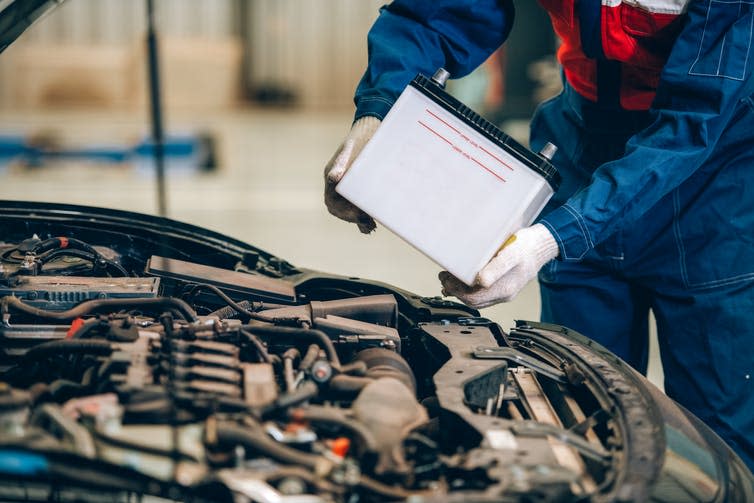 A mechanic fits a large, white battery into a car's chassis.