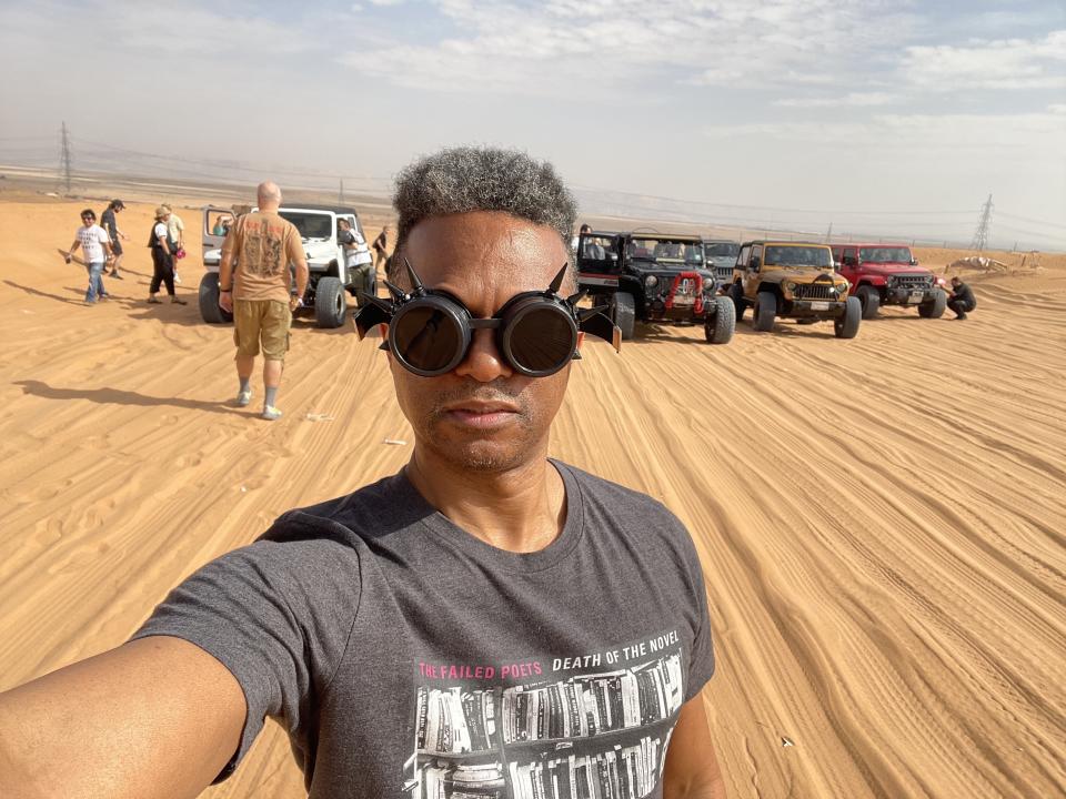 Writer Miles Marshall Lewis in the desert near Riyadh, Saudi Arabia for Soundstorm EDM Festival fun. With jeep trucks in the sand behind him.