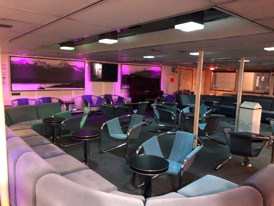 An empty bar and lounge area on a ferry ship with purple mood lighting.