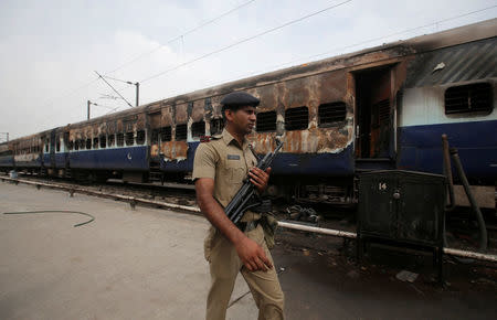 A security personnel member walks past a burnt carriage of a train near a railway station in New Delhi, India, August 26, 2017. REUTERS/Adnan Abidi