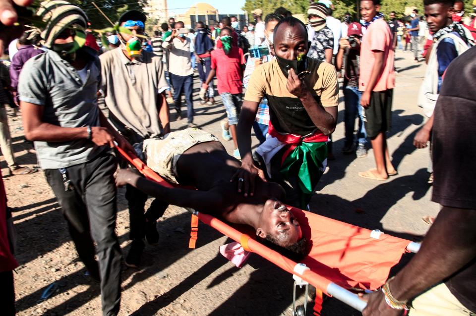 TOPSHOT - Sudanese youths carry away a fellow protester from the scene of confrontations with security forces, in the capital Khartoum on December 25, 2021, during a demonstration demanding civilian rule. Thousands of Sudanese protesters rallied two months after a military coup, demanding soldiers 