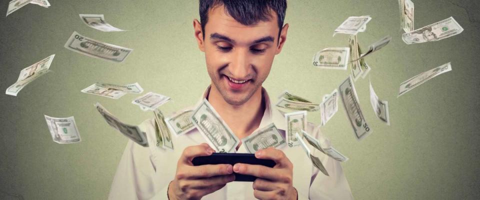 Happy young man using smartphone with dollar bills flying away from screen