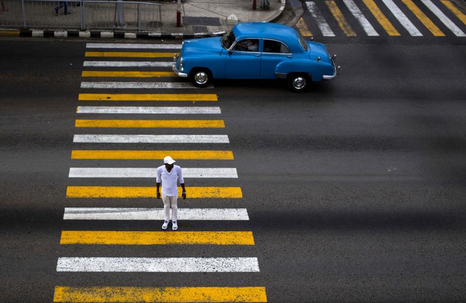 FILE - In this Nov. 16, 2018 file photo, a man uses the cross walk where the drivers passes in his classic car in Havana, Cuba. (AP Photo/Desmond Boylan, File)