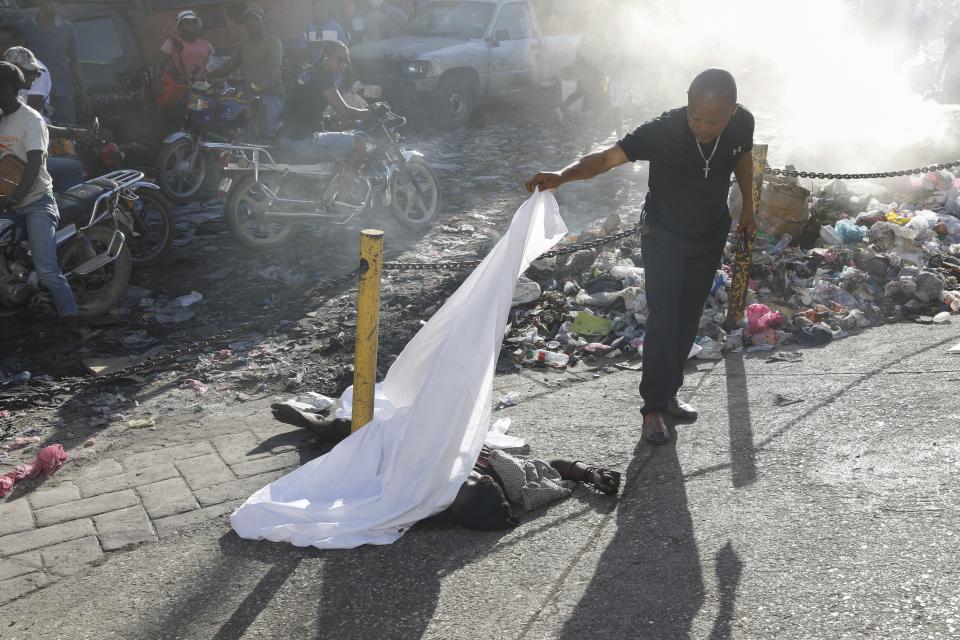 A person lifts a sheet to look at the identity of a body lying on the ground after an overnight shooting in the Petion Ville neighborhood of Port-au-Prince, Haiti, Monday, March 18, 2024. (AP Photo/Odelyn Joseph)