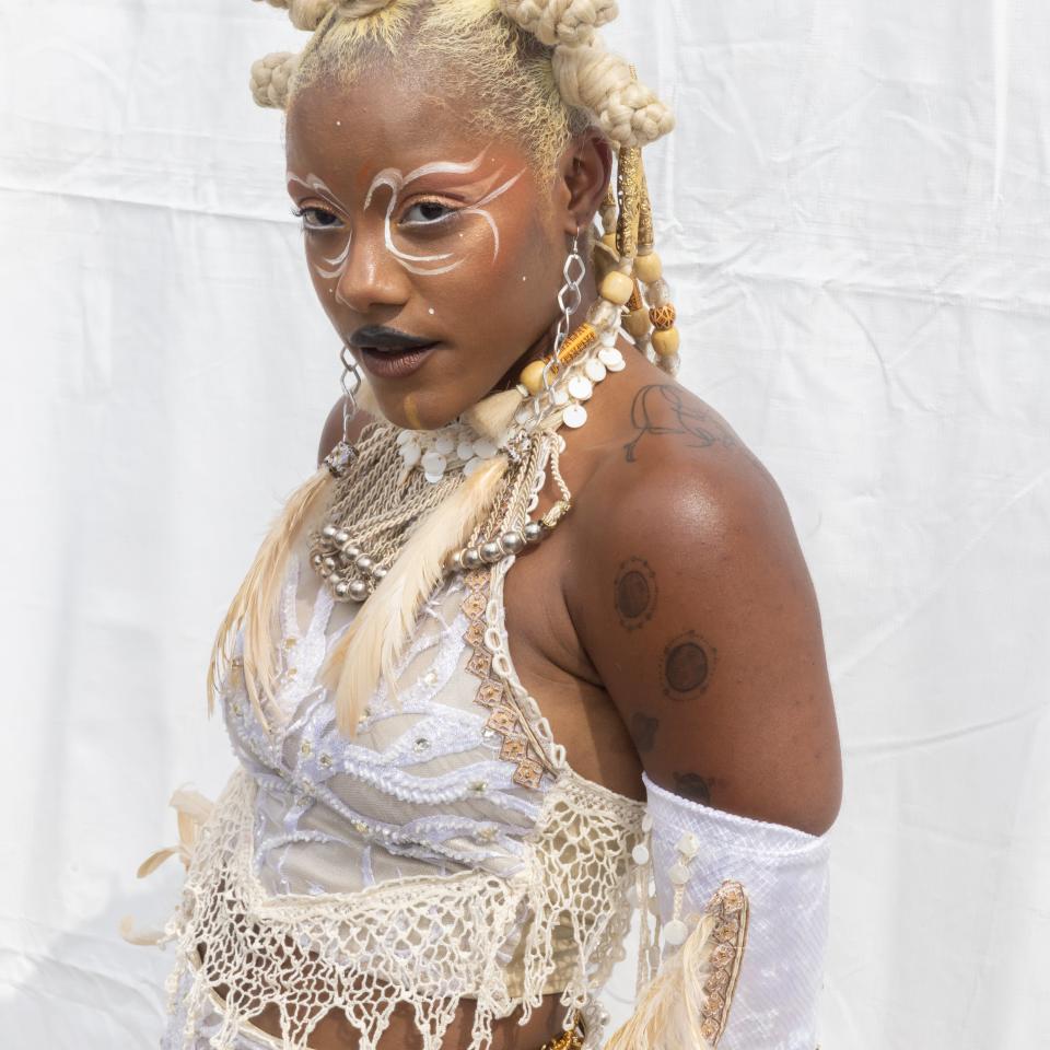 Iniko with dramatic eye makeup, blonde braided locks, and a lacy webbed halter-neck outfit at a media event