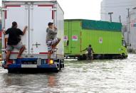 Workers stand at the back of a truck driving through a road flooded at an area affected by land subsidence and rising sea levels in North Jakarta