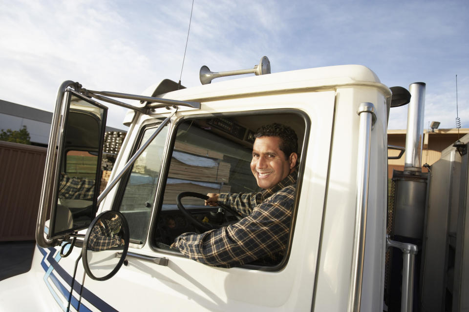 A truck driver smiling out the window of his cab