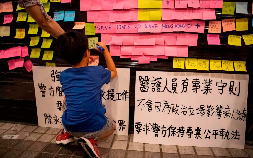 A boy writes on a Lennon Wall at a protest held by medics in the Central District of Hong Kong - AFP
