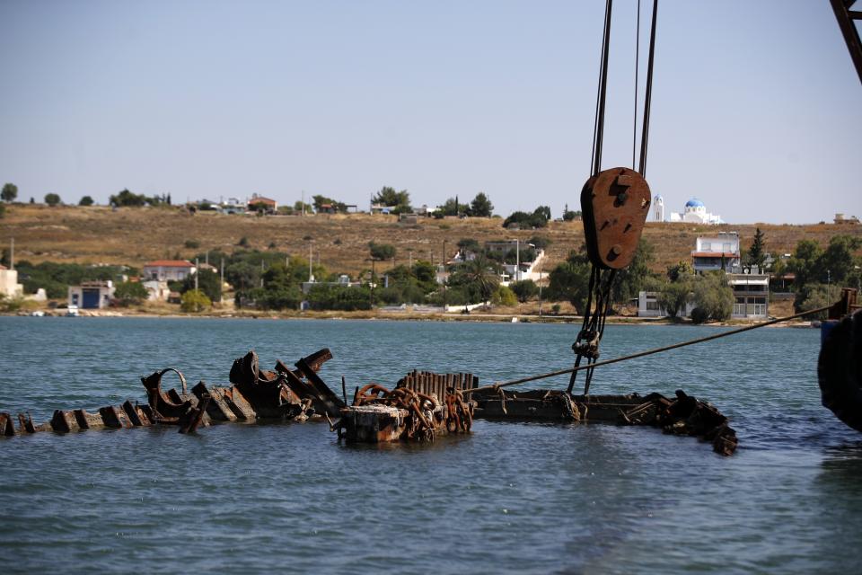 A floating crane holds a shipwreck before the raising operation on Salamina island, west of Athens, on Wednesday, June 29, 2020. Greece this year is commemorating one of the greatest naval battles in ancient history at Salamis, where the invading Persian navy suffered a heavy defeat 2,500 years ago. But before the celebrations can start in earnest, authorities and private donors are leaning into a massive decluttering operation. They are clearing the coastline of dozens of sunken and partially sunken cargo ships, sailboats and other abandoned vessels. (AP Photo/Thanassis Stavrakis)