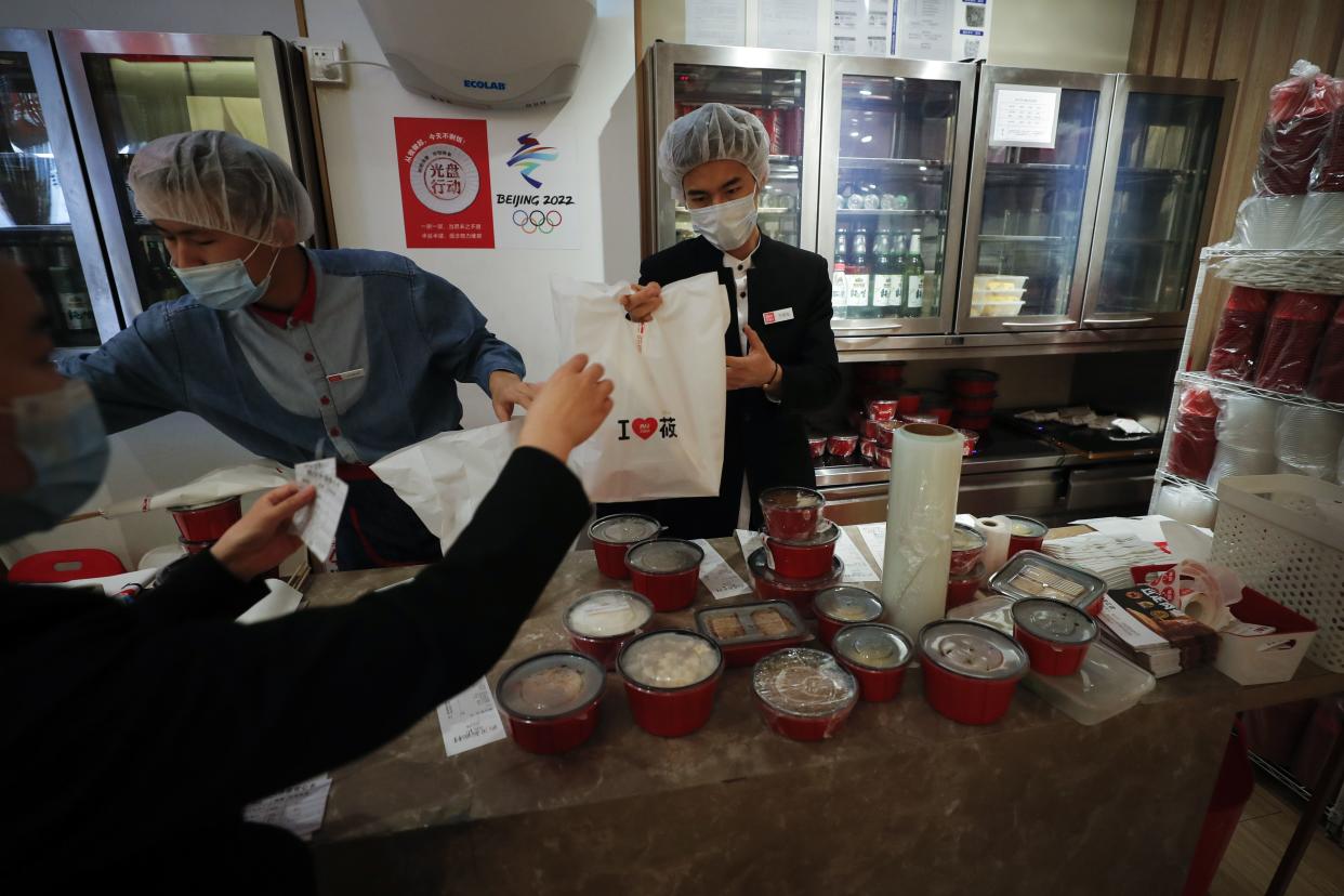 Workers wearing protective face masks and head covers pack food orders for takeout at the Xibei restaurant inside a shopping mall in Beijing on March 24, 2020.