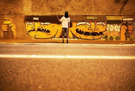 A "pichador", a graffiti artist who tags buildings and landmarks with angular, runic fonts, poses for a photograph in front of a mural of a Brazilian artist "Humanos", on a street in Sao Paulo, Brazil, April 11, 2017. The two faces on the mural are in reference to a "pichador" (L) and a graffiti artist. REUTERS/Nacho Doce