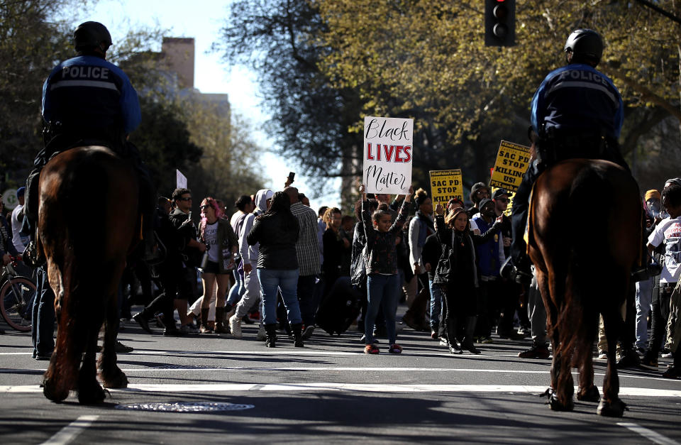 A young girl holds a Black Lives Matter sign in front of Sacramento police officers on horseback.