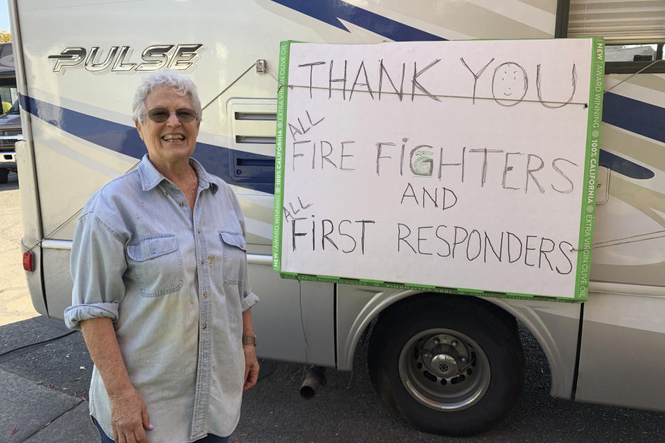 Lynn Darst shows a sign she hung on her motor home where she and her husband stayed after they were evacuated from their house in Windsor, Calif., Thursday, Oct. 31, 2019. Darst and her husband were camped out in their motor home on the edge of their seats for four days wondering if their house would survive yet another wildfire menacing Sonoma County. Flames had come close to their neighborhood of spacious homes surrounding by vineyards two years ago and the danger was closing in again. "We were comfortable, but fearful of what the consequences could be," Darst said Thursday, the day after finding her home had been spared once again. (AP Photo/Terry Chea)