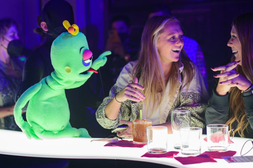 A green puppet talks to two women sitting at the bar at Superfrico at the Cosmopolitan Resort in Las Vegas, Nevada