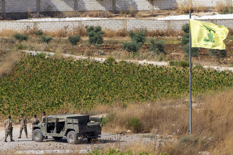 Lebanese soldiers next to a Hezbollah flag patrol in the southern Lebanese village of Aitaroun, on the Israel-Lebanon border, Israel, Tuesday, Aug. 27, 2019. Israeli forces along the border with Lebanon are on high alert, raising fears of a repeat of the 2006 war. (AP Photo/Ariel Schalit)