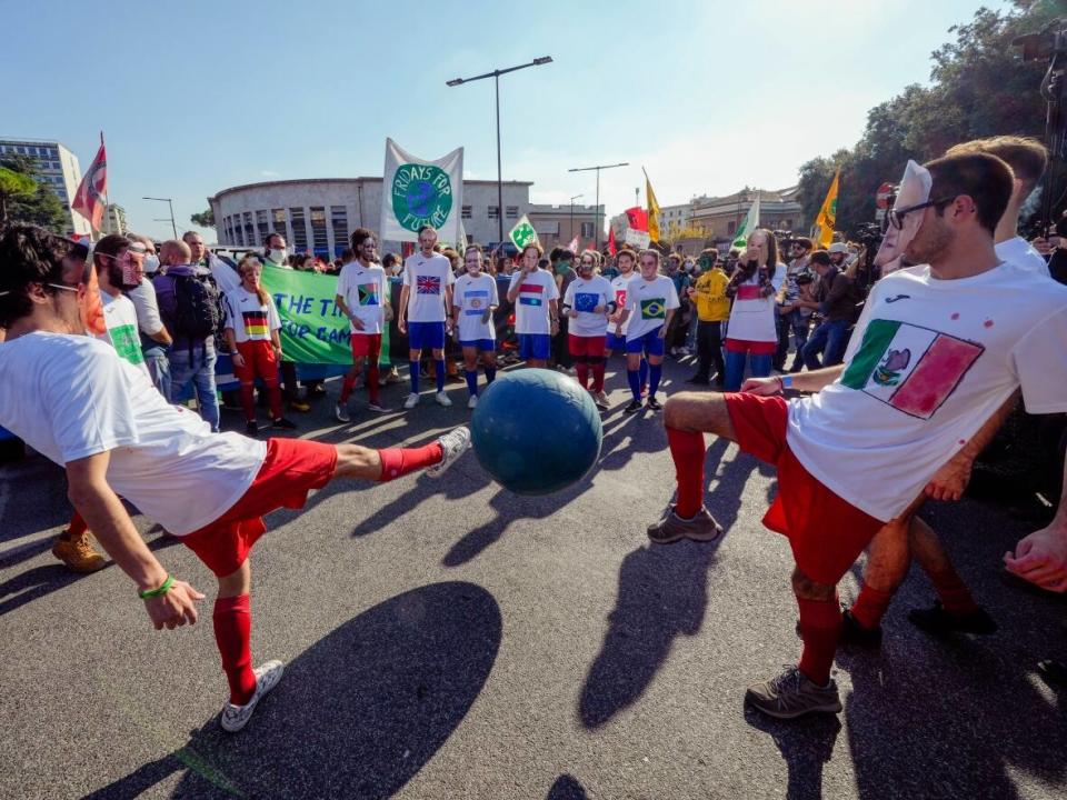 Demonstrators wearing cut-off masks with faces of world leaders stage a mock soccer game with a ball symbolizing the planet Earth during a march in Rome in October. Neither Canada nor the world appear on track to hit their climate goals. (Luca Bruno/The Associated Press - image credit)