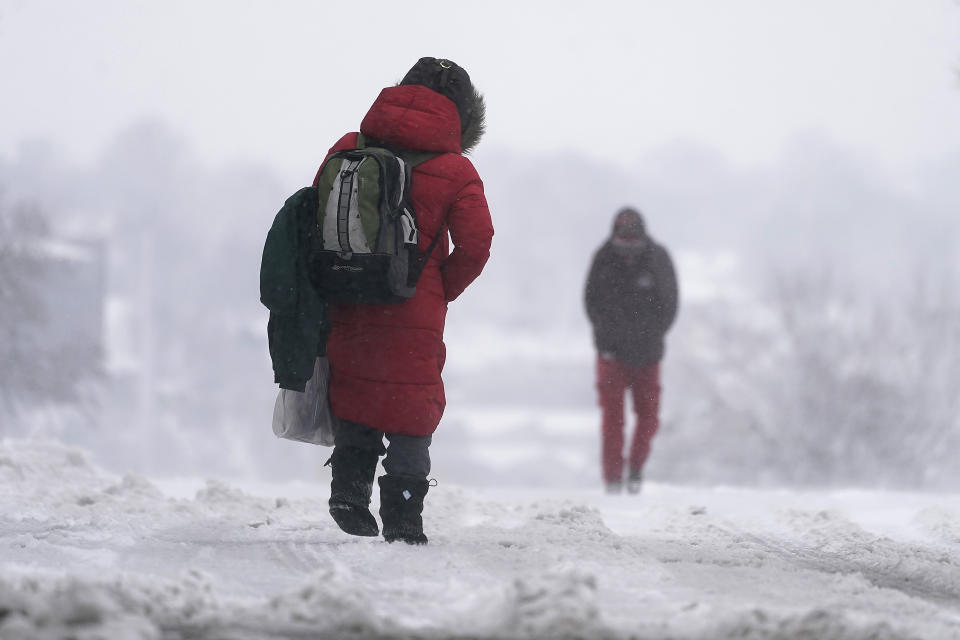 People walk down a snow-packed street as a winter storm moved through the region, Tuesday, Jan. 9, 2024, in Kansas City, Mo. (AP Photo/Charlie Riedel)
