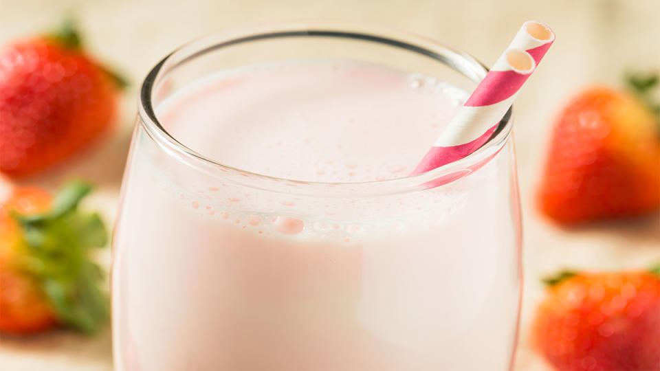 A glass of strawberry horchata (a rice-based chilled drink) on a table surrounded by fresh strawberries