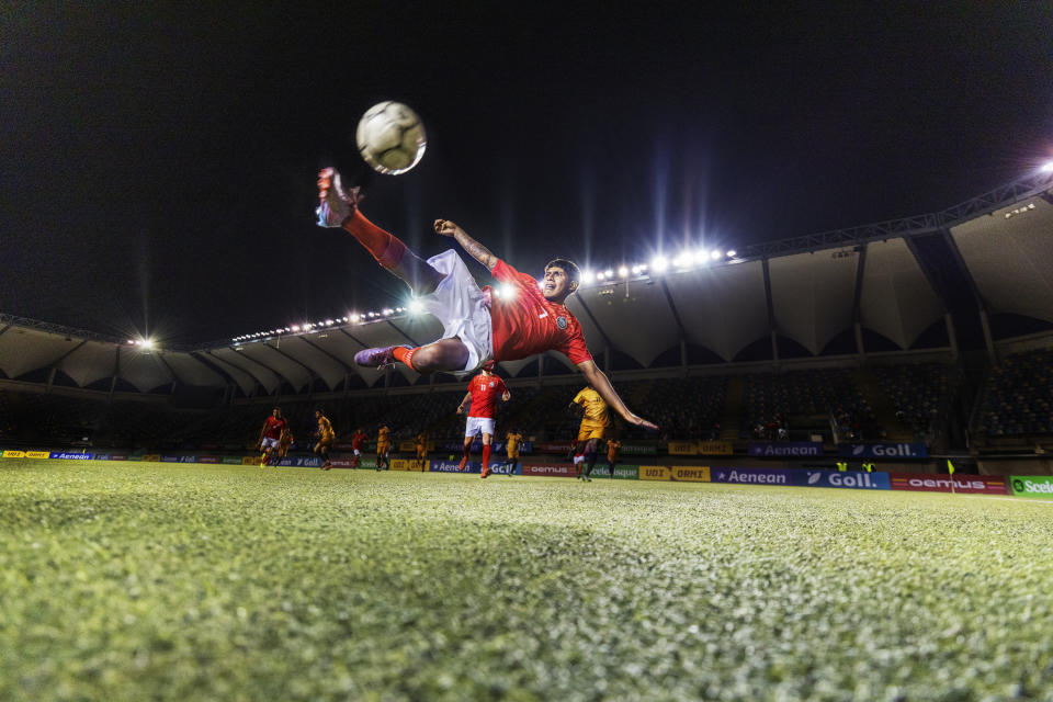 Toma amplia desde ángulo bajo de un joven jugador profesional de fútbol que salta habilidosamente y realiza una chilena en el aire, iluminado por las luces del estadio durante un partido internacional de fútbol.