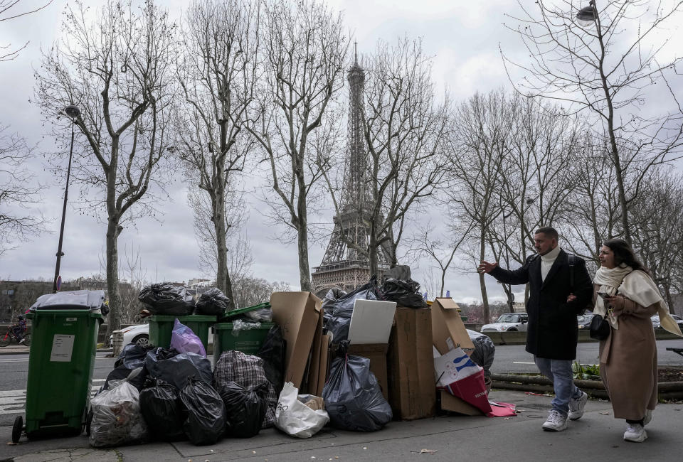 ARCHIVO - Gente pasa junto a un montón de basura cerca de la Torre Eiffel de París, el 12 de marzo de 2023, mientras continúa la huelga de los servicios de limpieza. (AP Foto/Michel Euler, Archivo)