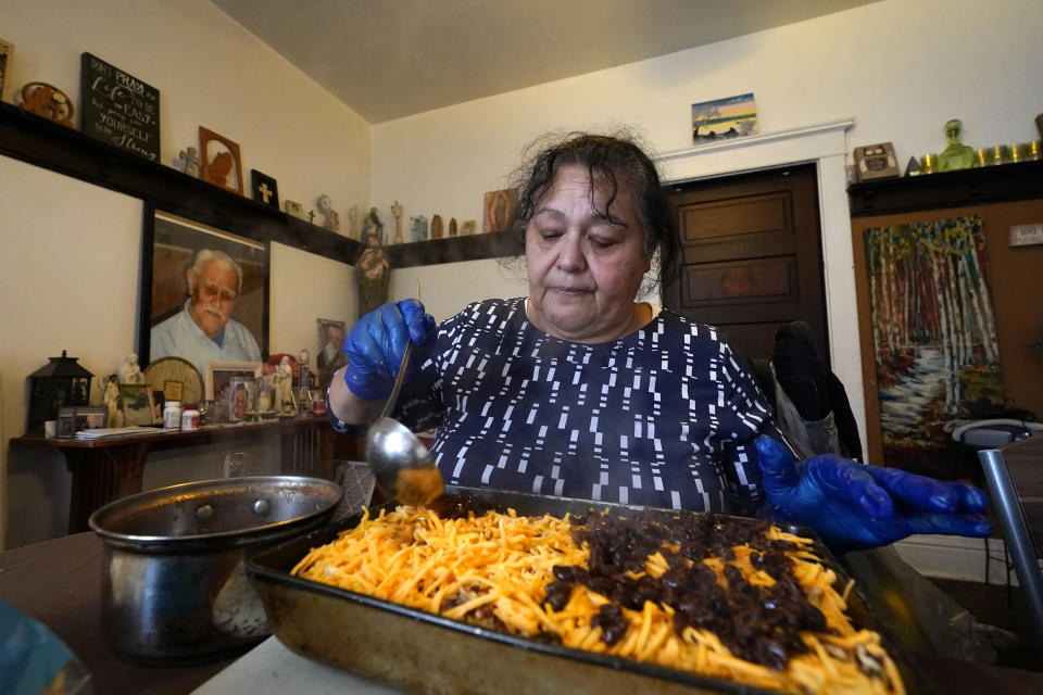 With a portrait of her deceased father on the wall behind, Olga Garcia prepares capirotada, a bread pudding layered with cheese, bananas, raisins, cinnamon and pecans, while preparing an afternoon family meal Wednesday, Nov. 4, 2020, in her home in Sedro-Woolley, Wash. On any other Thanksgiving, dozens of Olga's family members would squeeze into her home for the holiday. But this year, she'll deliver food to family spread along 30 miles of the North Cascades Highway in Washington state. If the plan works, everyone will sit down to eat in their own homes at precisely 6:30 p.m. and join a group phone call. (AP Photo/Elaine Thompson)