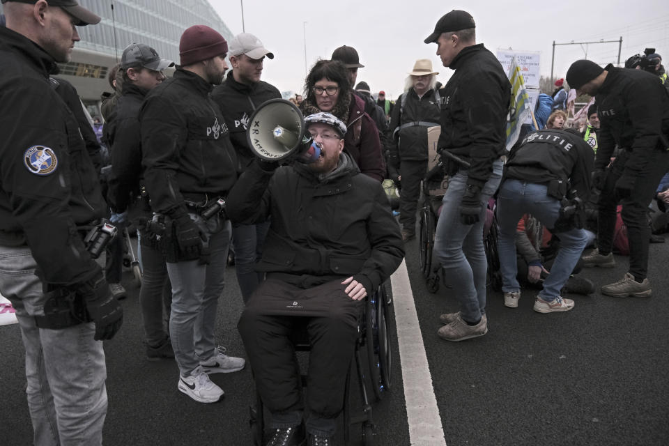 A climate activist keeps using his megaphone while being detained by police for blocking the main highway around Amsterdam near the former headquarters of a ING bank to protest its financing of fossil fuels, Saturday, Dec. 30, 2023. Protestors walked onto the road at midday, snarling traffic around the Dutch capital in the latest road blockade organized by the Dutch branch of Extinction Rebellion. (AP Photo/Patrick Post)