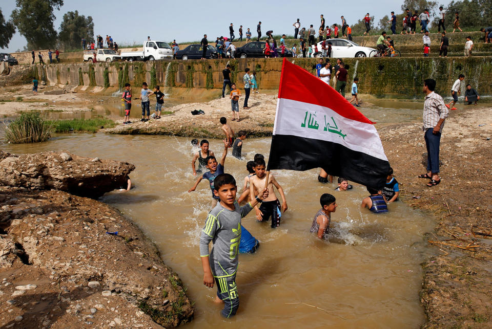 A boy holds the Iraqi flag as he plays in the water in Mosul