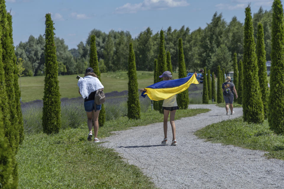 A girl uses a Ukrainian flag to shelter from the sun in Dobro Park, Motyzhyn, Kyiv region, Ukraine, Wednesday, June 26, 2024. Despite hardships brought by war flowers fill Kyiv and other Ukrainian cities. Dobro Park, a 370-acre (150 hectare) privately-run garden and recreation area west of Kyiv, was rebuilt after the Russian attack and occupation that lasted for more than a month.(AP Photo/Anton Shtuka)