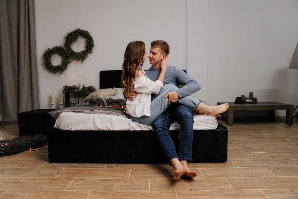 A young couple in love gently hugs on the bed at the eve of Christmas