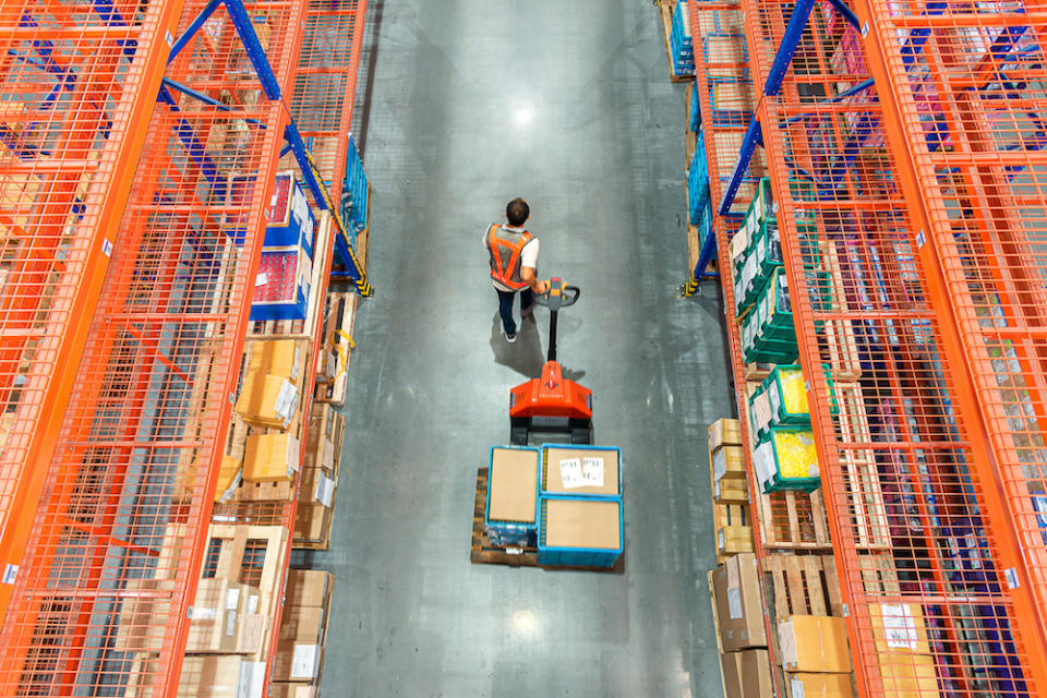 High angle view of Male warehouse worker pulling a pallet truck at distribution warehouse.