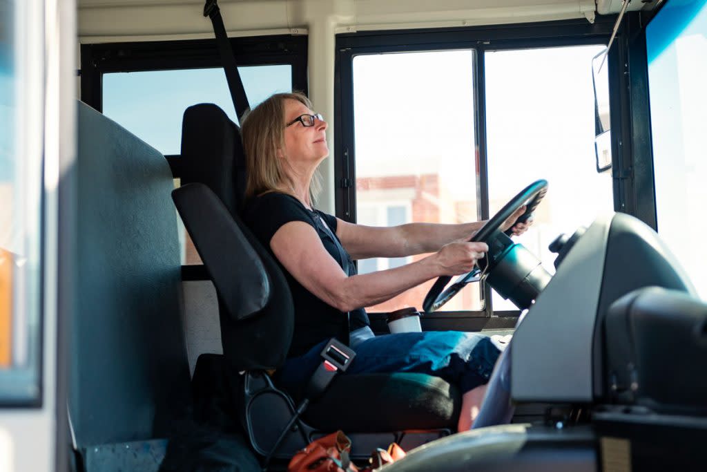 A senior woman drives a school bus.