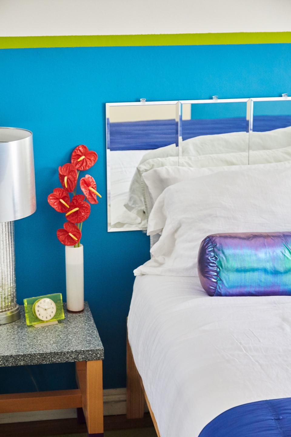 In Leah’s bedroom, a Soviet-era vintage green clock (an Etsy find) sits atop a Corian-topped bedside table (a Craiglist find), next to a headboard made of mirrors that she bought online and mounted on the wall. The only semi-splurge was the holographic bolster pillow, a custom piece.
