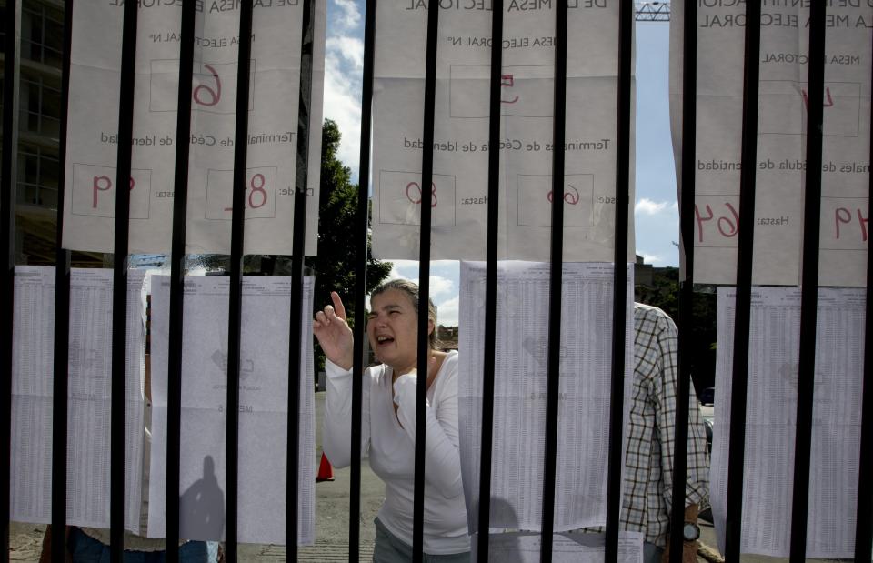 A voter looks for her voting station on a list outside of a polling station in Caracas, Venezuela, Sunday, Dec. 9, 2018. Venezuelans head to the polls Sunday to elect local city councils amid widespread apathy driven by a crushing economic crisis and threats of expulsion by opposition groups for candidates who participate in what they consider an "electoral farce." (AP Photo/Fernando Llano)