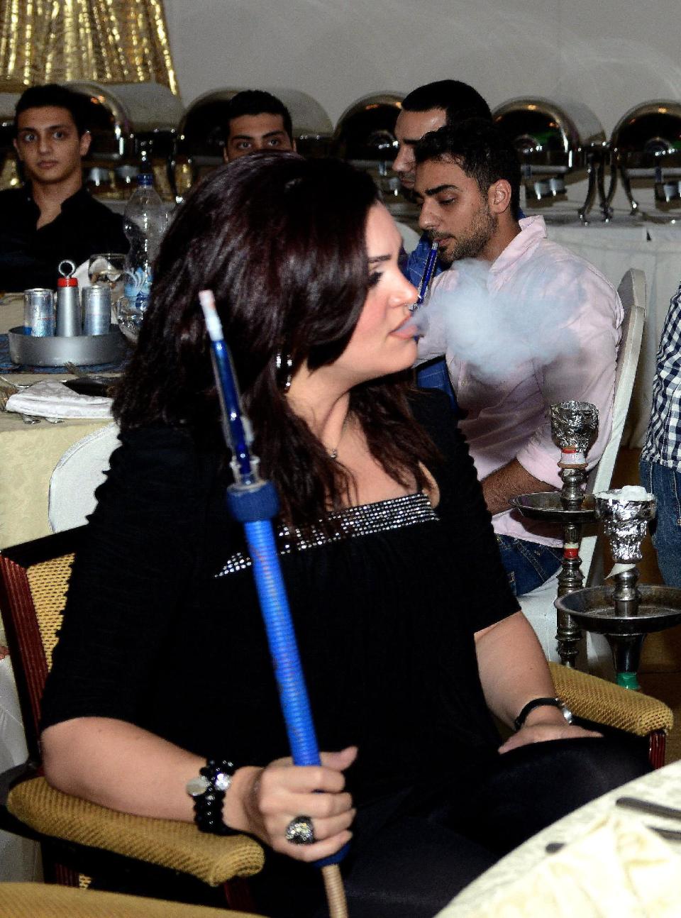 In this Monday, July 22, 2013 photo, an Arab woman smokes a water pipe during the holy Islamic month of Ramadan at a restaurant in Kuwait. One of the most traditional pleasures of the Middle East, leisurely puffing on a water pipe filled with aromatic tobacco _ has become ensnared in another of the region's familiar backdrops: Islamic conservatives decrying what they see as liberal decadence. (AP Photo/Gustavo Ferrari)