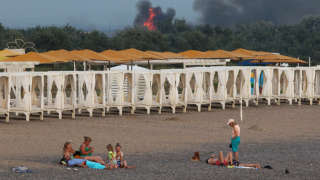 People rest on a beach as smoke and flames rise after explosions at a Russian military airbase, in Novofedorivka, Crimea August 9, 2022. REUTERS/Stringer     TPX IMAGES OF THE DAY