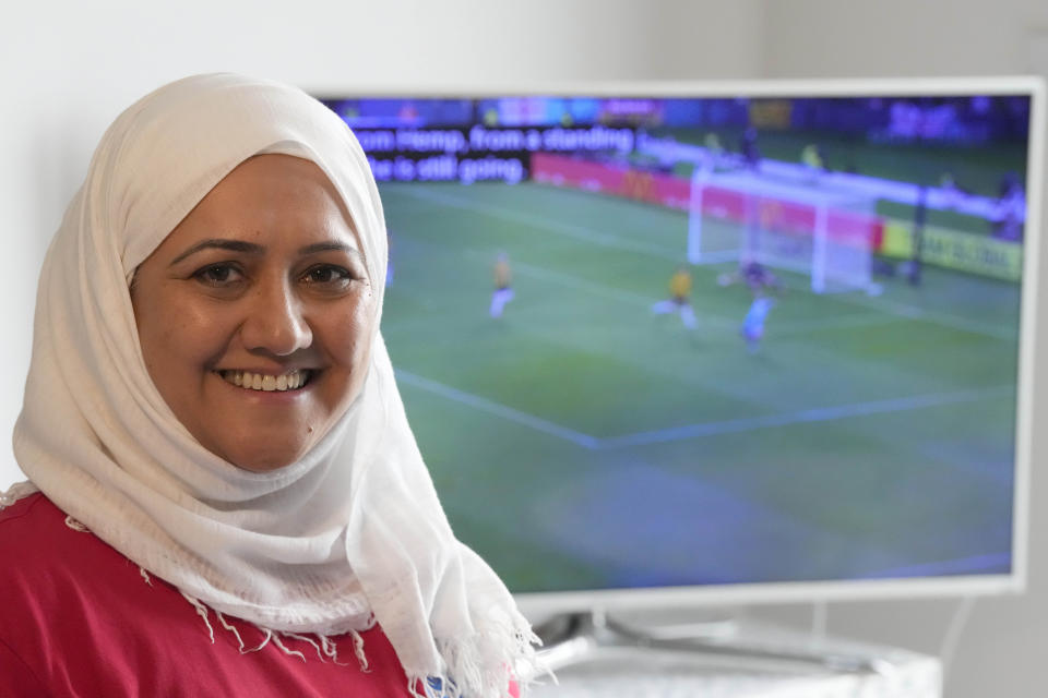 Huda Jawad smiles in front of her TV showing highlights of the Lionesses' last game, at her home, in London, Friday, Aug. 18, 2023. Jawad is a member of a fan group known as the Three Hijabis for their traditional Muslim headscarves, a group that campaigns against discrimination in football. (AP Photo/Frank Augstein)