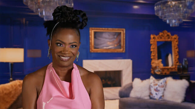 Kandi in an updo and pink latex dress sitting in a blue room.