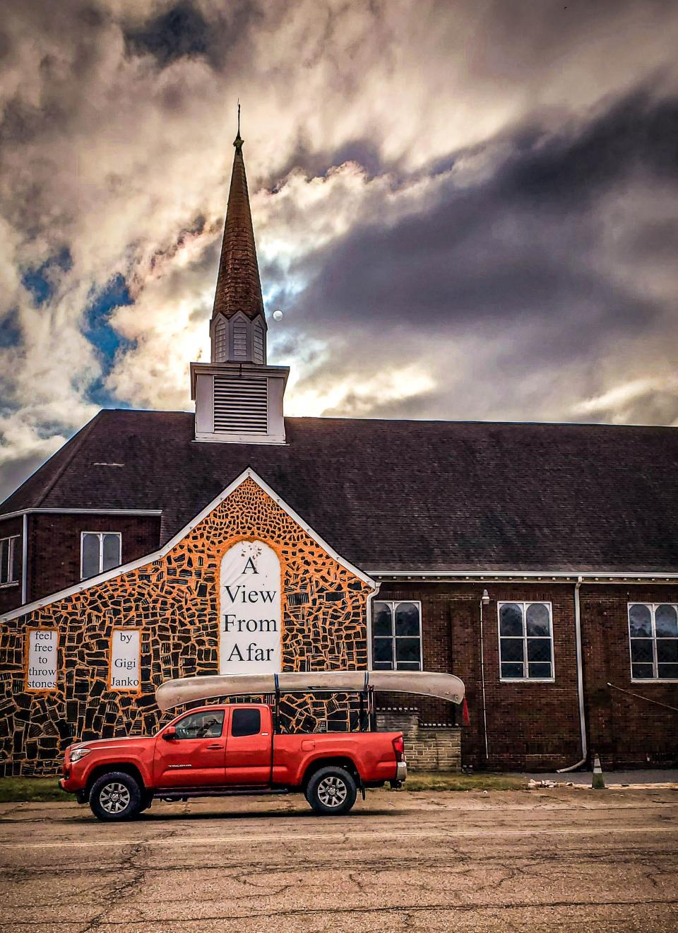 I parked my truck in front of a former church, now Gigi Janko’s studio and part of her artwork along the Ohio Riverfront in Wellsville. It was the sign on the left, inviting people to throw stones, that first got my attention. Under the overhanging canoe at the rear of the truck you can see jars of stones sitting atop stone walls.