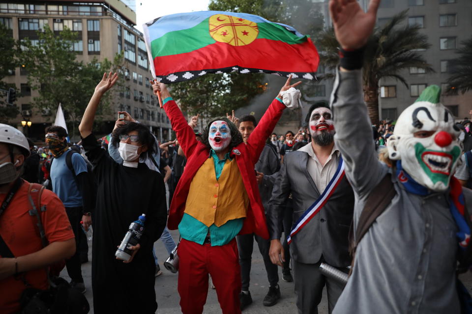 A man dressed as the Joker and holding a Mapuche flag cheers with others dressed in costumes during an anti-government protest in Santiago, Chile, Friday, Nov. 1, 2019. Chile has been facing days of unrest, triggered by a relatively minor increase in subway fares. The protests have shaken a nation noted for economic stability over the past decades, which has seen steadily declining poverty despite persistent high rates of inequality. (AP Photo/Rodrigo Abd)